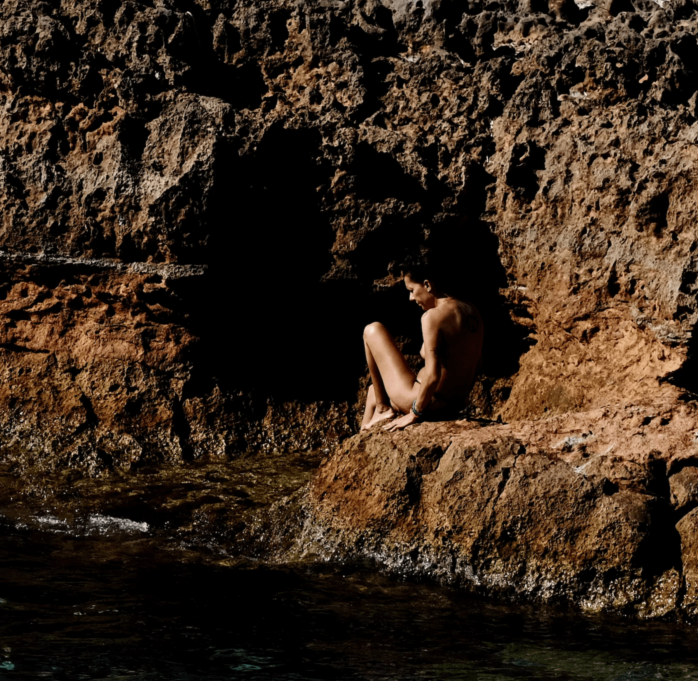 Photo d'une femme assise sur de la roche à la mer - Cécile Rosenstrauch