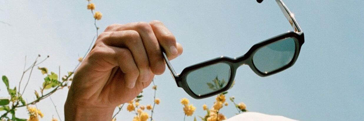 Photo ensoleillée, un homme tient une paire de lunettes jimmy fairly en main