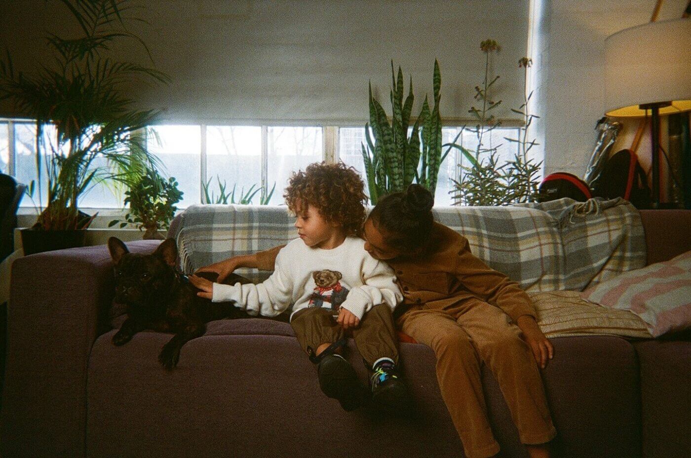 Two kids are sitting on the couch and petting a dog