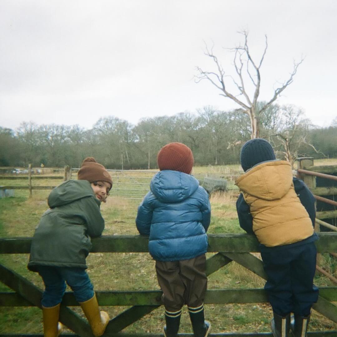 3 enfants sont se dos, agrippés à la barrière d'un pré