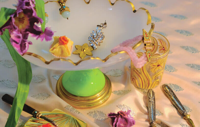 une coupelle, des couverts et des bijoux dorés sont posés sur une table, une lumière douce et chaude les éclaire