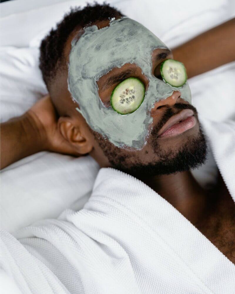 homme se relaxant avec un masque sur le visage et des concombre posé sur les yeux